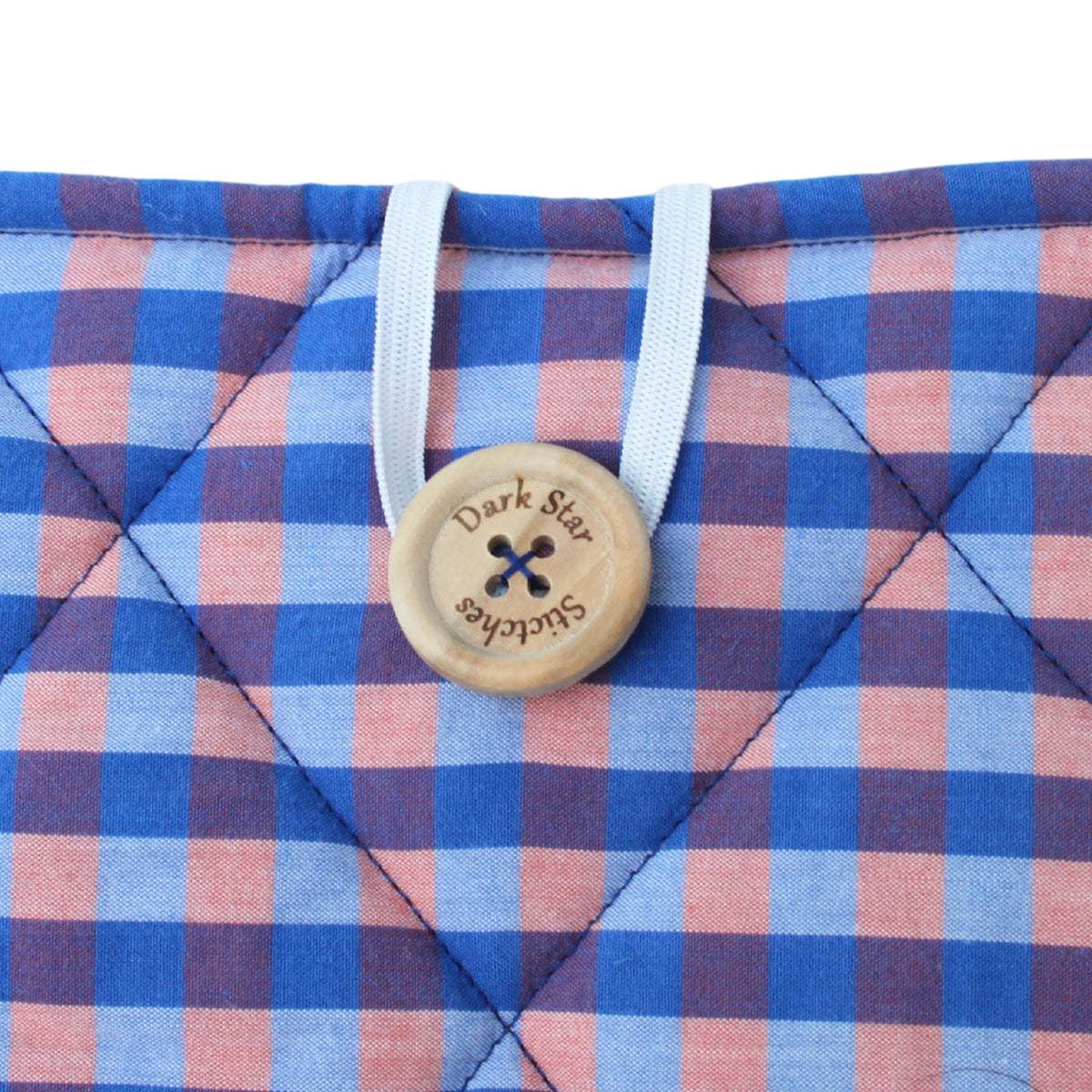 Close-up of button closure on handmade quilted booksleeve in orange and blue check fabric