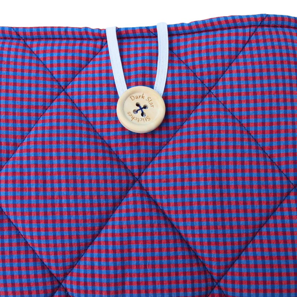 Close-up of button closure on handmade quilted booksleeve in red and blue check fabric