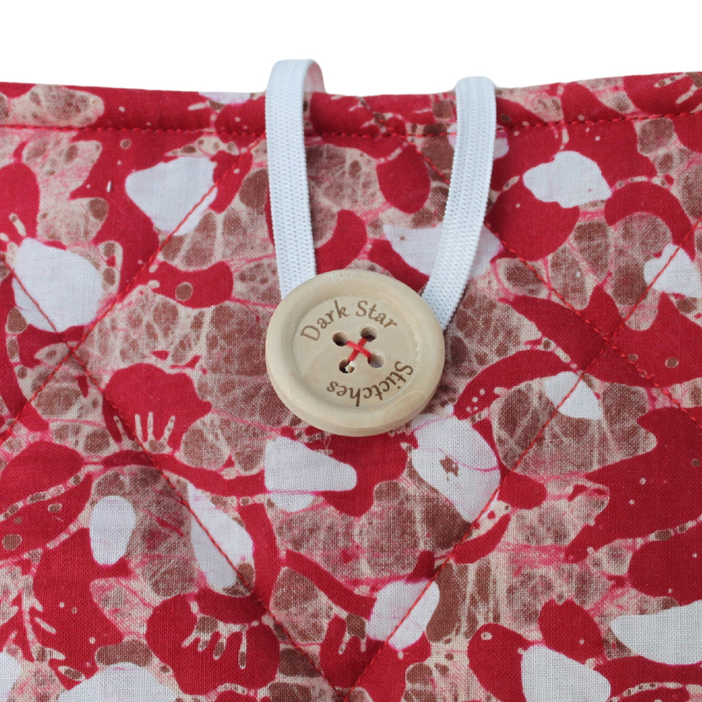 Close-up of button closure on handmade quilted booksleeve in red, brown and white patterned fabric