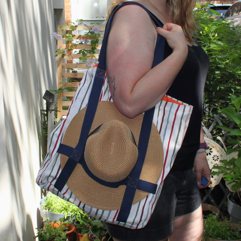Hat holder strap in use on handmade fabric tote bag in multi-colour stripes with orange lining and navy strap — Dark Star Stitches