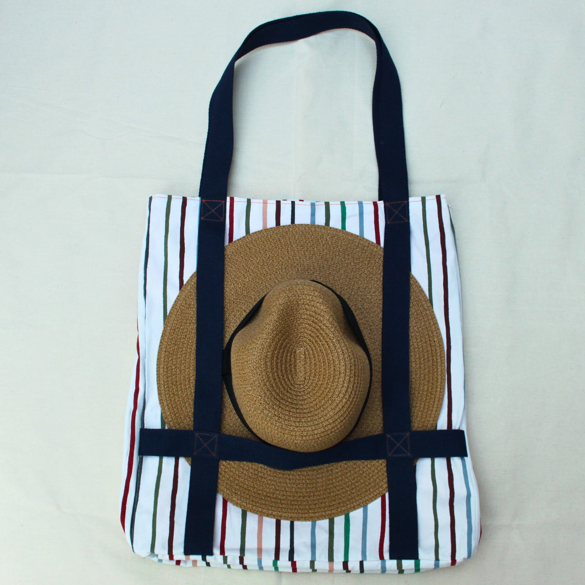 Hat holder in use on handmade fabric tote bag in multi-colour stripes with blue lining and navy strap — Dark Star Stitches