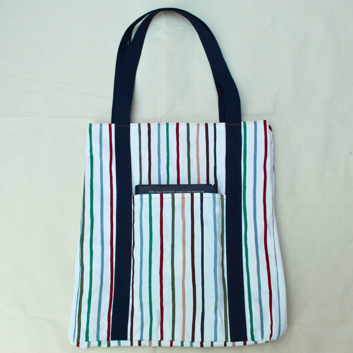 Pocket in use on handmade fabric tote bag in multi-colour stripes with orange lining and navy strap — Dark Star Stitches