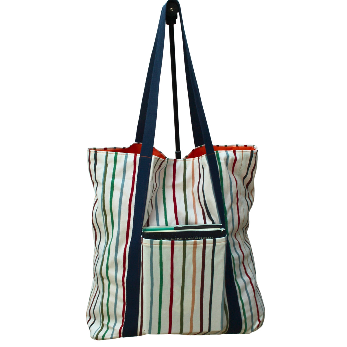 Rear view in use of handmade fabric tote bag with hat holder in multi-colour stripes with orange lining and navy strap — Dark Star Stitches