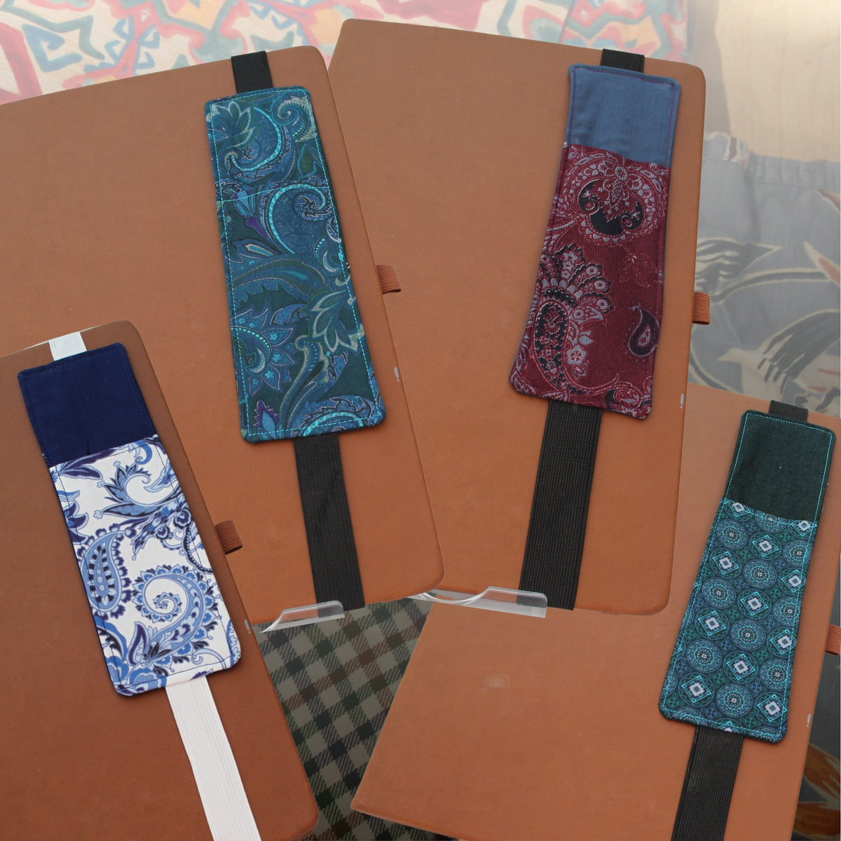 Four handmade A4 fabric notebook pen pockets clipped onto tan notebooks, made from pre-loved paisley, floral, gingham and geometric fabrics in blue, teal, burgundy and green — Dark Star Stitches Second Chapter collection