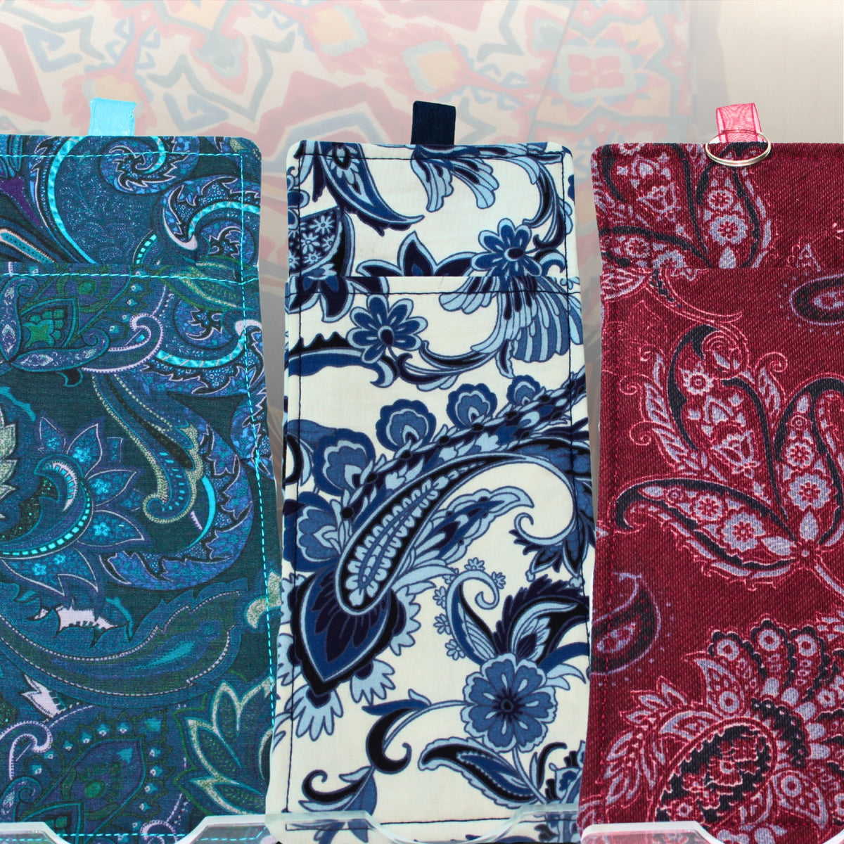 Three handmade double-sided lanyard pockets side by side, made from pre-loved paisley and floral fabrics in teal, blue and white, and burgundy — Dark Star Stitches Second Chapter collection